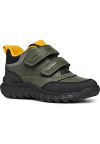 Scarpe impermeabili verdi con chiusure in velcro, dettagli gialli, suola in gomma nera e parte superiore testurizzata per una migliore aderenza. Progettate per l'uso all'aperto.