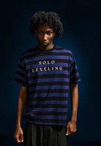 Černo-modré proužkované tričko s krátkými rukávy, na hrudi nápis "SOLO LEVELING" v bílé barvě. Materiál bavlna, volný střih.