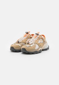Beige og kremfargede sneakers med teksturert overdel, oransje detaljer og en kraftig svart såle. Har et snøresystem med lås og logo-detalj.