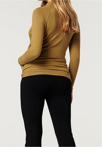 Dlouhý rukáv, přiléhavý top v hořčicové barvě vyrobený z měkké tkaniny, doplněný černými legínami. Hladká textura a jednoduchý design.