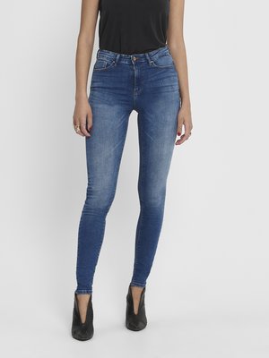 Džíny s vysokým pasem, modré skinny vyrobené z denimu, s klasickým pětikapsovým designem a mírným vyblednutím, kombinované s černými botami na podpatku.