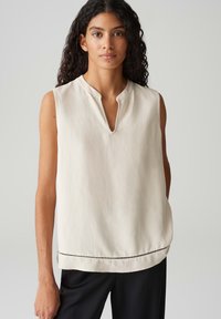 Ärmellose cremefarbene Bluse mit V-Ausschnitt, ausgestattet mit einem dezenten Saum-Muster, aus leichtem Stoff, lockerer Passform und glatter Textur.