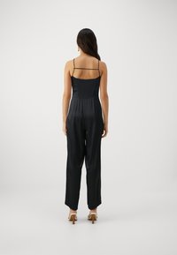 Svart satin jumpsuit med en åtsittande smockad bodice och tunna band, med vida, flödande ben och en jämn textur.