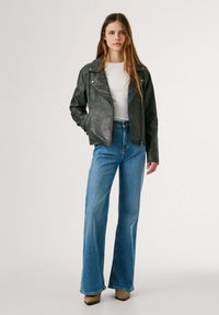 Must matte nahk mootorrattajope, millel on sobiv disain, lukuga sulgemine ja nurga all olevad kraed. Koos kõrge vöökohaga laienevate siniste teksade ja beežide kontsadega.