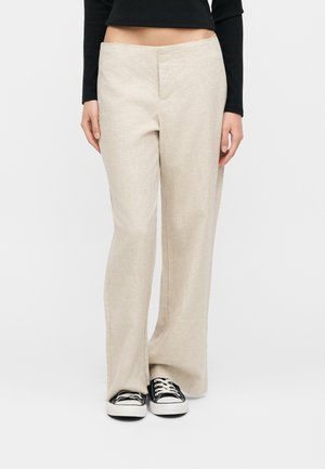 Μπεζ παντελόνι με φαρδιά μπατζάκια, φορεμένο με μαύρο crop top μακριάς μανίκας και ασπρόμαυρα αθλητικά παπούτσια, εμφανιζόμενο από τη μέση έως τα πόδια σε λευκό φόντο.