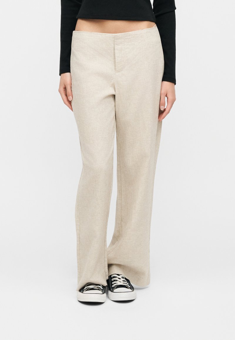 Μπεζ παντελόνι με φαρδιά μπατζάκια, φορεμένο με μαύρο crop top μακριάς μανίκας και ασπρόμαυρα αθλητικά παπούτσια, εμφανιζόμενο από τη μέση έως τα πόδια σε λευκό φόντο.