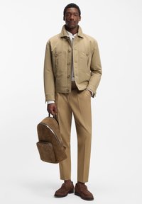 Bēša kokvilnas jaka ar priekšējām kabatām, kopā ar bēšām biksēm. Apģērbu noslēdz brūna zamšāda mugursoma un apavi.