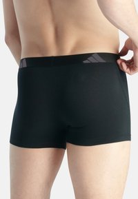 Svarta atletiska boxerkalsonger tillverkade av stretchtyg. Har en logotyp på midjebandet och en slät yta. Designen är figurnära.