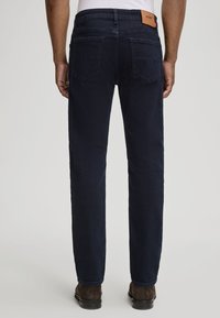 Granatowe dżinsy o prostym kroju, tylne kieszenie z dekoracyjnym przeszyciem oraz brązowa skórzana naszywka w pasie.