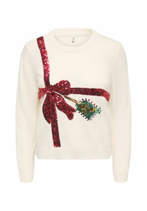 Pull crème avec nœud en sequins rouge et étiquette cadeau verte sur le devant, à manches longues et col rond.