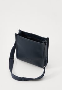 Sac à main en cuir marine avec une finition texturée, de forme rectangulaire, fermeture à zip en haut et une bandoulière ajustable estampillée du nom de la marque.