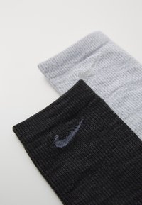 Kaks paari lühikesi sokke: üks hall ja teine must, mõlemad ribatekstuuriga. Igal sokil on kontrastse värviga väike Nike logo.