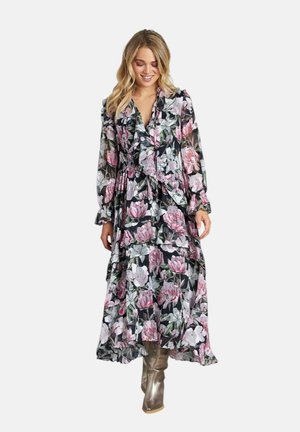 Vestido maxi floral en negro con flores rosas y blancas, con volantes en las capas, mangas largas y un escote en V profundo. Combinado con botas metálicas hasta la rodilla.