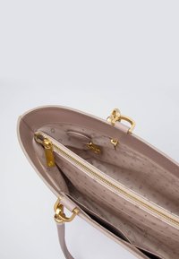 Borsa a mano rosa chiaro con esterno in pelle liscia, accessori in oro e scomparto con zip. L'interno presenta un motivo con logo e diverse tasche.