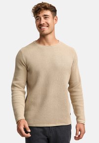 Beige gebreide trui met een gestructureerd patroon, ronde halslijn en lange mouwen. Heeft een subtiele zoomdetail en een iets getailleerde pasvorm.