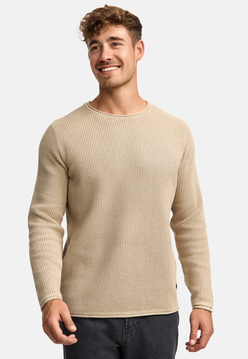 Beige gebreide trui met een gestructureerd patroon, ronde halslijn en lange mouwen. Heeft een subtiele zoomdetail en een iets getailleerde pasvorm.