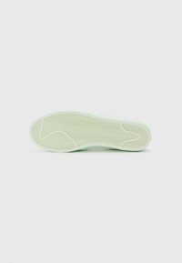 Semelle de chaussure en caoutchouc vert présentant un motif en chevrons, une texture lisse et un design à bout arrondi. Style minimaliste sans accents supplémentaires.