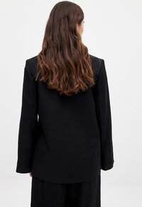 Black blazer with a smooth texture, slightly oversized design, notched lapels, and a single vent at the back. Long sleeves with tailored fit.