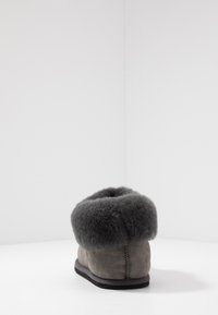 Zapatilla de ante gris con un puño de pelo gris esponjoso y texturizado, suela plana y una costura que recorre la parte trasera como detalle adicional.