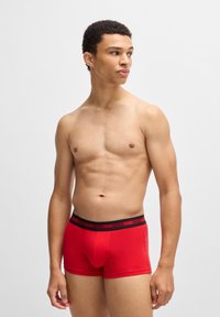 Bóxer rojo de tela suave con una cinturilla negra que presenta el nombre de la marca "HUGO". Diseñado para un ajuste ceñido y comodidad.