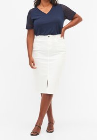 Mörkblå V-ringad topp med spetskortärmar, kombinerad med en vit knälång jeanskjol med en framfåra och fem fickor. Svarta remsandaler.