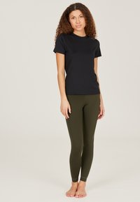 Black short-sleeve t-shirt paired with fitted olive green leggings. T-shirt features a round neckline; leggings have a smooth, stretchy texture.