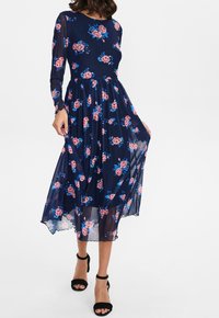 Vestido midi floral en azul marino con mangas largas transparentes, que presenta rosas rosas y acentos azules, un corpiño ajustado y un dobladillo acampanado.