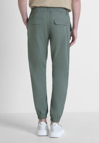 Groene joggingsbroek met elastische tailleband en opgerolde enkels, met twee achterzakken. Gecombineerd met witte sneakers. Gladde stof textuur.