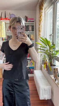 Black fitted T-shirt with a V-neck design, made of smooth fabric. Notable sleeves and subtle embellishments along the bottom edge.