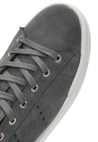 Baskets en cuir gris avec des lacets gris, œillets ronds et semelle en caoutchouc blanche. Texture lisse avec des coutures subtiles et des détails de perforation.