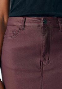 Taille et partie supérieure de la cuisse d'une personne portant un pantalon mauve et un haut noir côtelé, mettant en avant les détails des boutons, de la fermeture éclair et des poches.