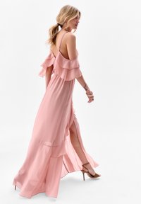 Lange roze chiffon jurk met gelaagde ruffles op de mouwen, een hoge split en dunne schouderbandjes. Gladde textuur, vloeiende ontwerp.