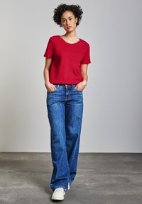 Rode t-shirt met korte mouwen, ruime pasvorm. Gecombineerd met blauwe wijde jeans en witte sneakers. Eenvoudig ontwerp, geen zichtbare patronen of hardware.