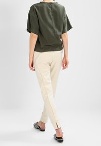 Dark green short-sleeved blouse; cream tapered pants with side slits; black flat sandals; minimalistic design, soft textures.