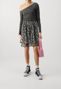 Haut gris décolleté, jupe noire à fleurs avec volants, baskets montantes noires, et sac à main rose. Mélange de textures et de motifs.