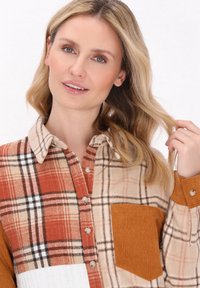 Rutig skjorta med en blandning av beige, orange och svarta färger, med knäppning framtill, en bröstficka och olika tygtexturer.