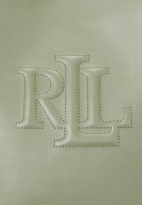 Zaļas ādas materiāls ar uzspiestajiem "RL" inicialiem. Iezīmē kontrastējošas brūnas šuvju malas un logotipa detaļas.