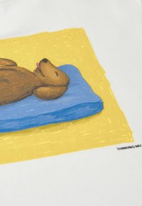 Chien brun dormant avec la langue sortie, reposant sur un oreiller bleu sur fond jaune sur un tissu blanc.