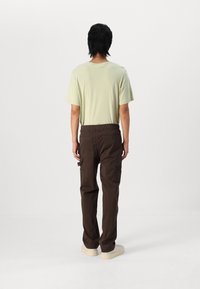 Ljusgrön t-shirt med korta ärmar och bruna cargobyxor med sidofickor. T-shirten har en avslappnad passform, medan byxorna har ett elastiskt midjeband.