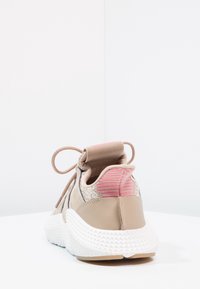 Beżowy but sportowy z teksturowanym tyłem, różowymi akcentami i białą gumową podeszwą. Posiada wyściełany kołnierz i kolorystycznie dopasowane sznurówki.