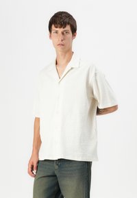 Kortærmet, hvid tekstureret skjorte med knaplukning foran og en klassisk krave, parret med mellemvaske denim jeans.