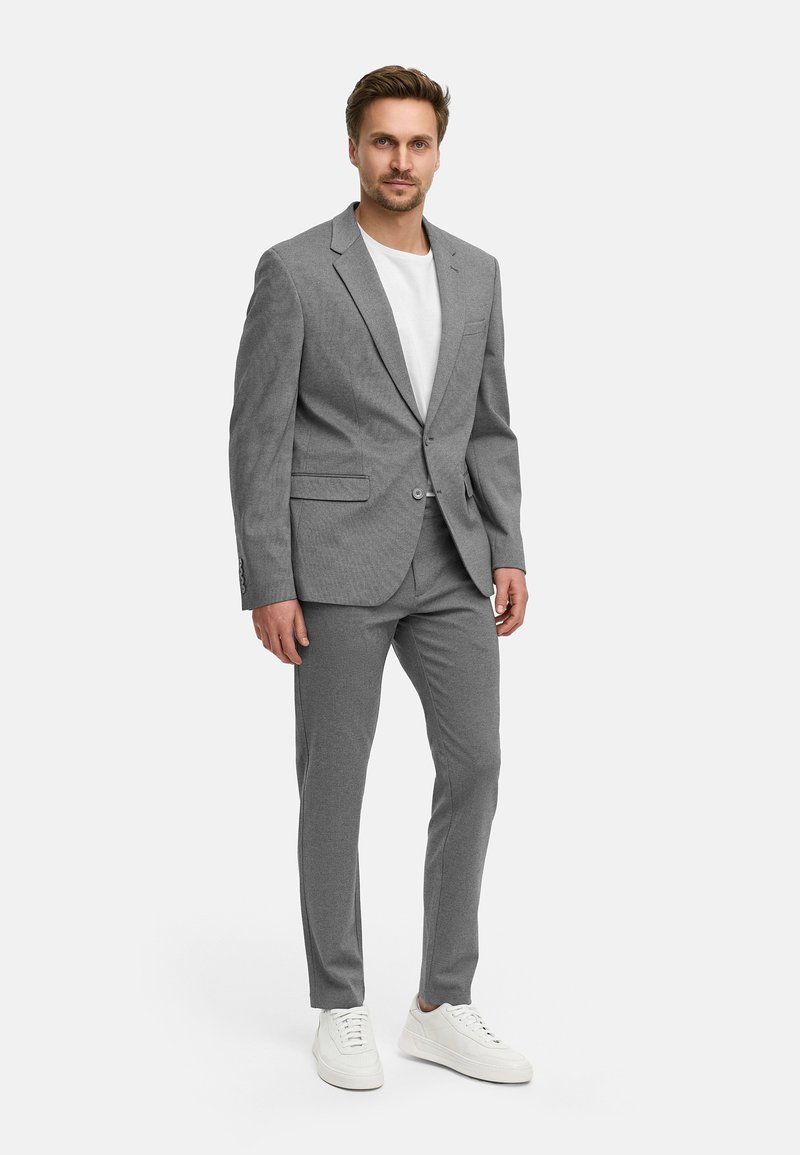 Grå tvådelad kostym med notchad slag, enkel knappstängning och smala byxor, tillsammans med en vit t-shirt och vita sneakers.