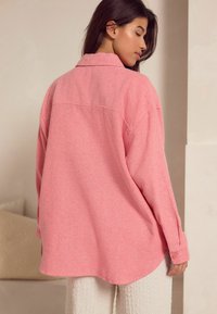 Roze oversized shirt van een textuurstof, met een kraag, knoopmanchetten en een ronde zoom, gecombineerd met lichte textuurpants.