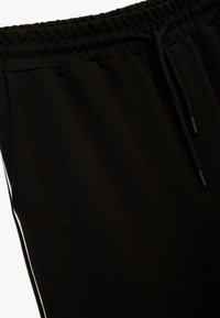 Schwarze sportliche Jogginghosen mit elastischem Bund, Kordelzug, seitlichen Taschen und weißen Streifenakzenten an den Seiten.