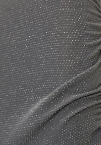 Šedá texturovaná látka se sklady, která je pokryta malými stříbrnými tečkami rovnoměrně rozmístěnými po povrchu. Jemná a hladká textura.