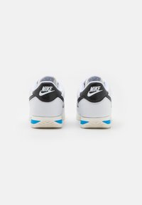 Scarpe Nike bianche con accenti neri, linguetta del tallone testurizzata e dettaglio blu sulla suola. Presentano un colletto imbottito e il logo sul retro.