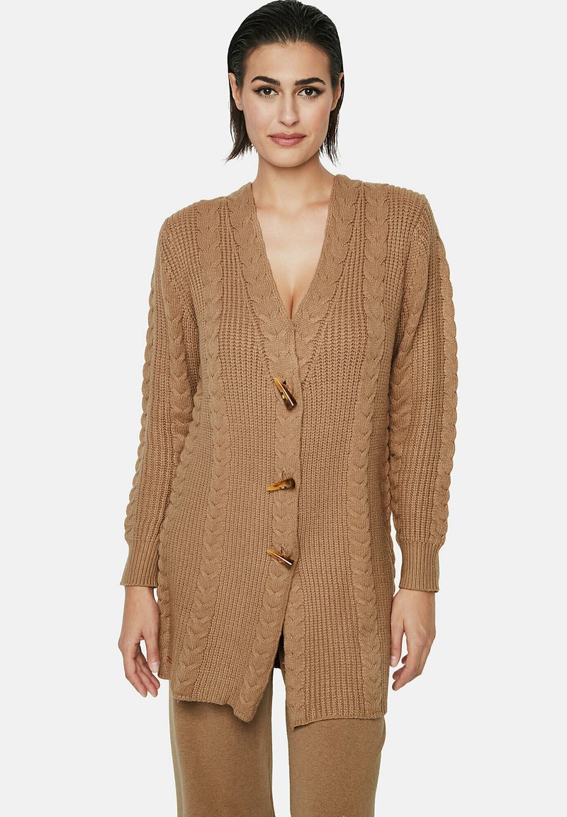 Cardigan en tricot beige avec un profond décolleté en V, trois gros boutons, des accents de motif en cable, et des manches longues avec des poignets côtelés.