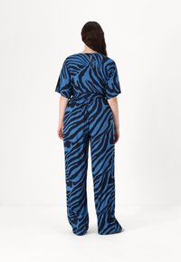 Zilas un melns zebra raksta kombinezons ar īsām piedurknēm, elastīgu jostasvietu un platiem kājām. Ievērojama atvēruma detaļa aizmugurē. Mīksta auduma tekstūra.