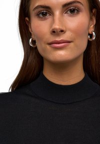 Haut noir à col montant en maille côtelée avec une finition texturée. Le modèle porte des boucles d'oreilles créoles en argent. Les cheveux sont lisses et tombent sur les épaules.