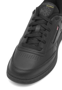 Čierne kožené tenisky s textúrovaným povrchom, perforovanou špičkou a čiernymi šnúrkami. Na jazyku sa nachádza zlaté logo "Reebok Classic".